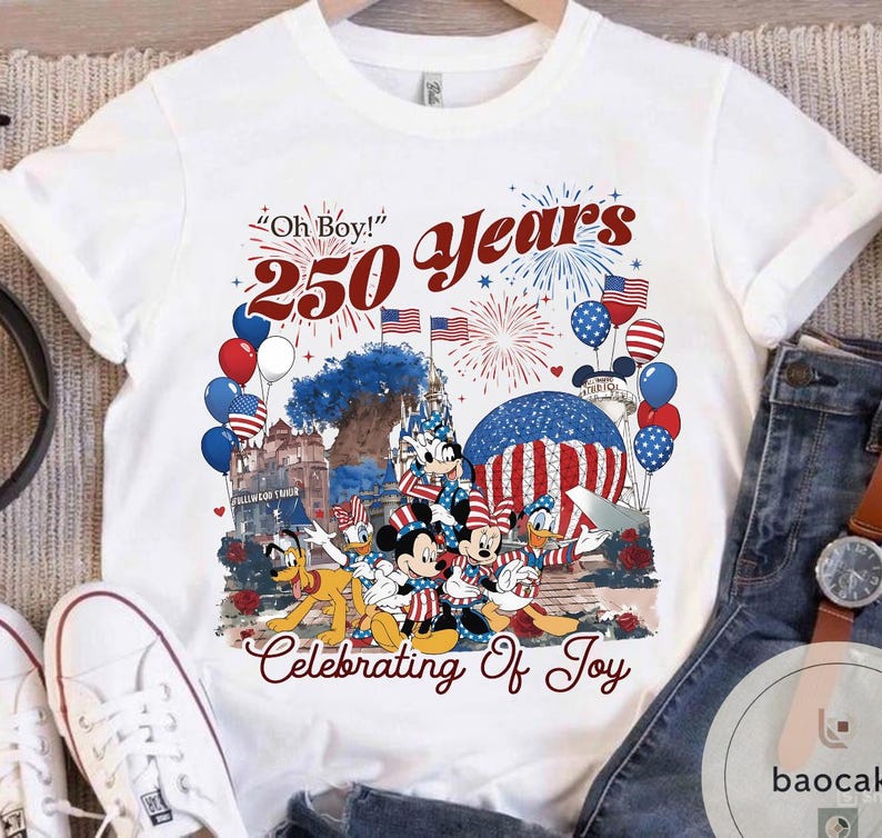 Puede incluir: Camiseta blanca con un gr&aacute;fico colorido que celebra 250 a&ntilde;os. El dise&ntilde;o presenta a Mickey Mouse, Minnie Mouse, Donald Duck y Pluto con atuendo patri&oacute;tico, junto con fuegos artificiales, globos y el texto "Oh Boy!" y "Celebrating Of Joy."