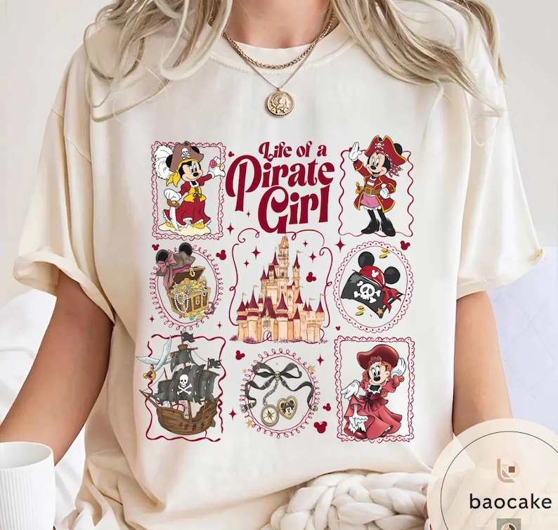 May include: Cream-colored t-shirt featuring a "Life of a Pirate Girl" design. The design includes cartoon illustrations of a pirate-themed character, a treasure chest, a pirate ship, and a castle, all framed in decorative borders.