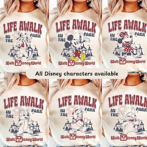 May include: Cream-colored sweatshirts with various Disney character graphics. Each shirt features the text "LIFE AWALK IN THE PARK" in burgundy, along with "Walt Disney World." The image also states "All Disney characters available."