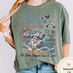 Puede incluir: Camiseta verde con un dise&ntilde;o de Disney Cruise Line. El gr&aacute;fico incluye un crucero, un faro y personajes de Disney como Mickey Mouse y Donald Duck. El texto dice "Disney Cruise Line Est 1998" y "The Most Magical Cruise On Earth."