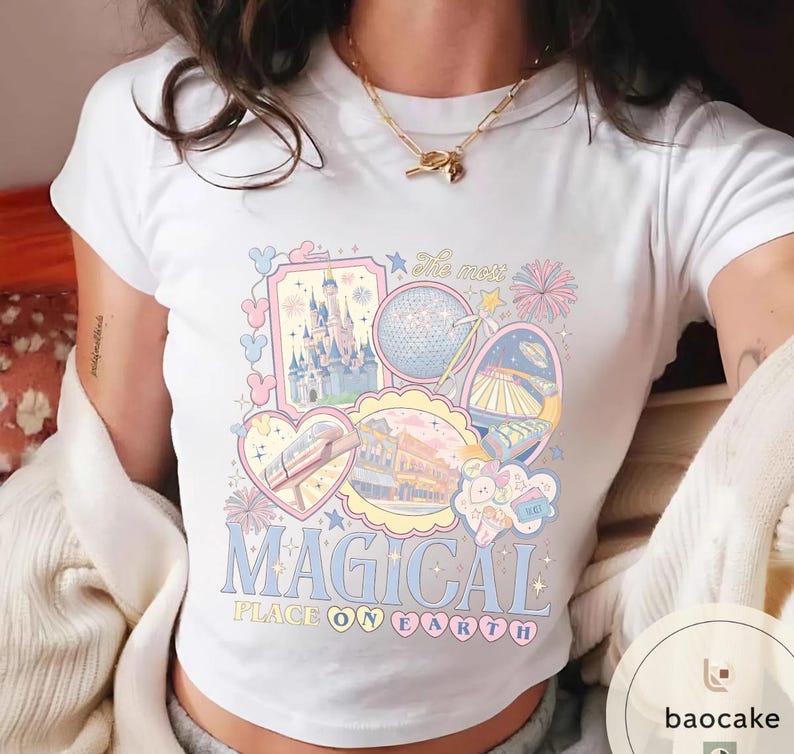 May include: White t-shirt with a colourful graphic featuring theme park icons, including a castle, a globe, and a monorail. The text "MAGICAL PLACE ON EARTH" is displayed in a playful font, with pastel colours.