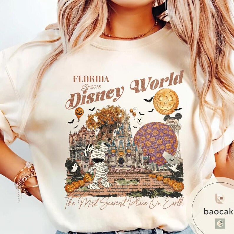 Op de afbeelding: Cr&egrave;mekleurige sweatshirt met een Halloween-thema Disney World-afbeelding. Het ontwerp toont een mummie Mickey Mouse, pompoenen, vleermuizen en de tekst "Florida Disney World Est. 2018" en "The Most Scariest Place On Earth."