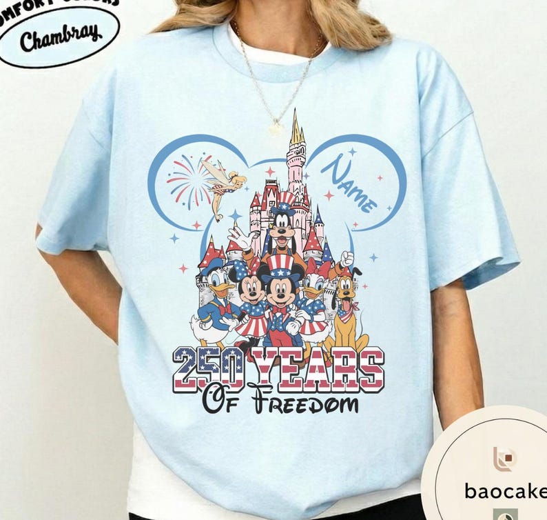 Peut inclure: T-shirt bleu clair avec un motif Disney repr&eacute;sentant des personnages devant un ch&acirc;teau, avec le texte "250 Years of Freedom". Le motif comprend Mickey Mouse, Donald Duck et d'autres personnages. Le mot "Name" est &eacute;galement visible.