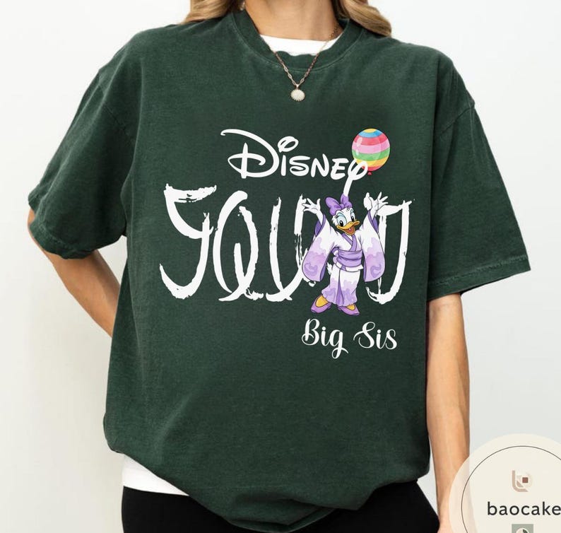 Puede incluir: Camiseta verde oscuro con la frase "Disney Squad" en blanco, con un dibujo de Daisy Duck con un kimono morado sosteniendo un globo arco&iacute;ris. Las palabras "Big Sis" est&aacute;n debajo.