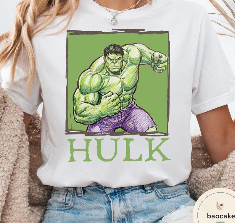 May include: White t-shirt featuring a green and purple illustration of the Hulk in a fighting pose, set against a green background. The word "HULK" is printed in green below the image.