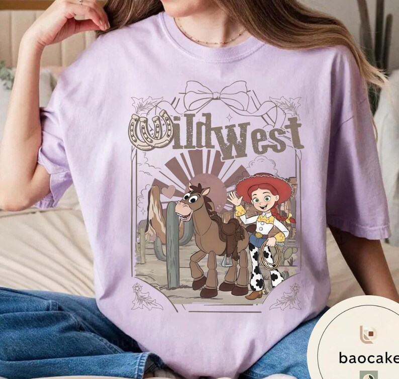 Pu&ograve; includere: T-shirt lilla chiaro con un design del Far West. La grafica include un cavallo dei cartoni animati, una cowgirl e la scritta "Wild West". Il design &egrave; ambientato in un deserto con cactus.