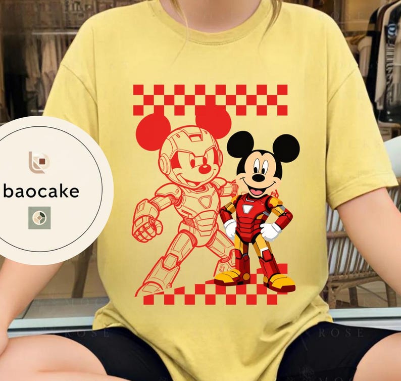 May include: A yellow t-shirt featuring a red and white checkered pattern and a graphic of Mickey Mouse in an Iron Man-inspired suit and another in a robotic suit. The shirt has short sleeves and a round neckline. The brand logo "baocake" is visible on the left side.