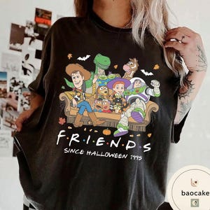 May include: A black t-shirt featuring a graphic of Toy Story characters sitting on a couch. The text reads F R I E N D S SINCE HALLOWEEN 1995. The design includes Woody, Buzz Lightyear, Jessie, Rex, Bullseye, and Mr. Potato Head with autumn leaves.
