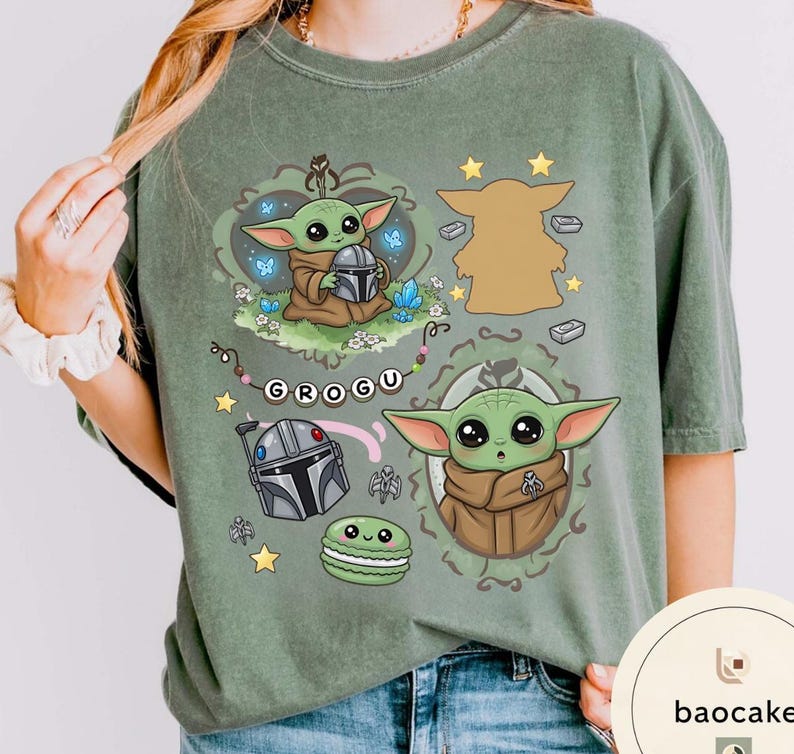 May include: A sage green t-shirt featuring a graphic print of the character Grogu in various poses, a silver helmet, a green macaron, and the text GROGU on a beaded string. The design includes small stars, blue butterflies, and crystals.