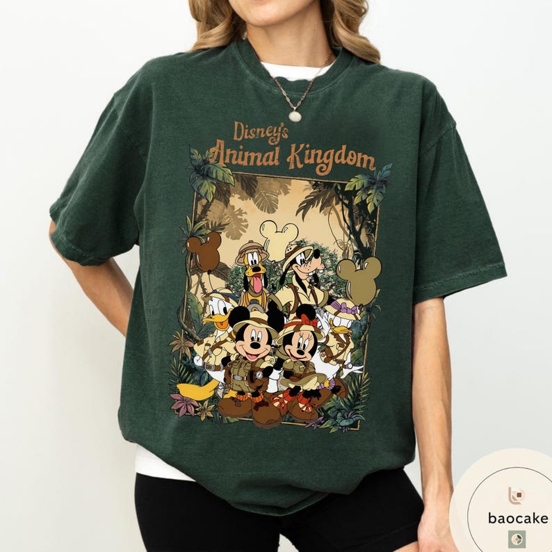 May include: Dark green t-shirt featuring a graphic of Disney's Animal Kingdom characters, including Mickey and Minnie Mouse, Donald Duck, Goofy, and Pluto. The design is framed with jungle foliage and the text "Disney's Animal Kingdom".