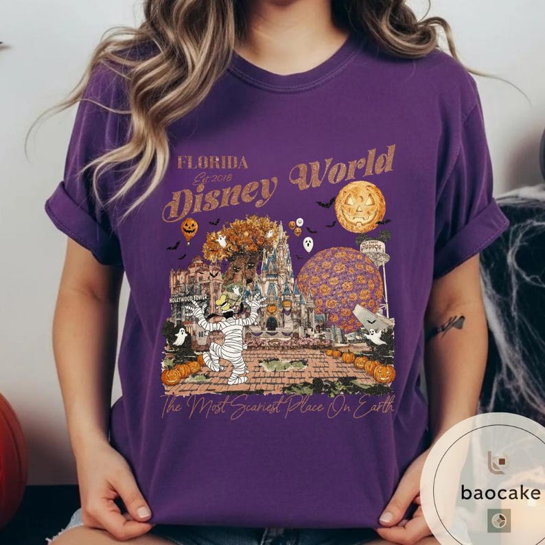 Op de afbeelding: Paars T-shirt met een Halloween-thema. Het ontwerp bevat de tekst "Florida Disney World Est 2016" met een griezelige sc&egrave;ne met een mummie, pompoenen en een spookkasteel. De zin "The Most Scariest Place On Earth" is ook opgenomen.