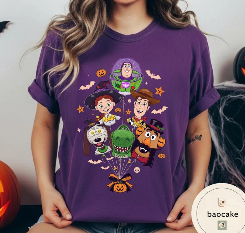 Pode incluir: Uma t-shirt roxa de manga curta com uma impress&atilde;o gr&aacute;fica de v&aacute;rias personagens animadas vestidas com fatos de Halloween, incluindo um ranger espacial, uma cowgirl, um cowboy, um c&atilde;o, um dinossauro e uma figura de batata.