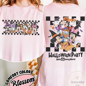 May include: Light pink t-shirt featuring a Halloween-themed graphic with cartoon characters. The front has a row of characters on a checkered background. The back displays the text "HALLOWEEN PARTY" and "Walt Disney World".