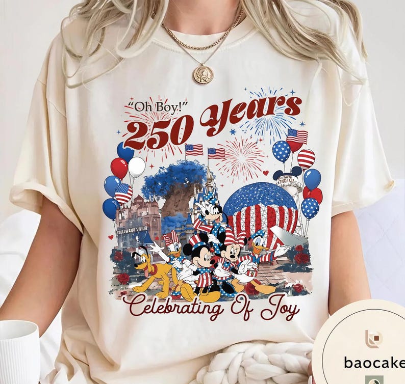 Puede incluir: Camiseta color crema con un gr&aacute;fico colorido que celebra 250 a&ntilde;os. El dise&ntilde;o incluye a Mickey Mouse, Minnie Mouse, Donald Duck y Pluto con atuendos patri&oacute;ticos, junto con globos, fuegos artificiales y el texto "Oh Boy!" y "Celebrating of Joy."
