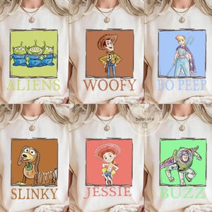 K&ouml;nnte beinhalten: Eine Kollektion von sechs cremefarbenen T-Shirts mit quadratischen Grafikdrucken von Toy Story-Figuren. Jedes T-Shirt zeigt eine Figur mit dem darunter gedruckten Namen: Aliens, Woody, Bo Peep, Slinky, Jessie und Buzz Lightyear in bunten K&auml;sten.