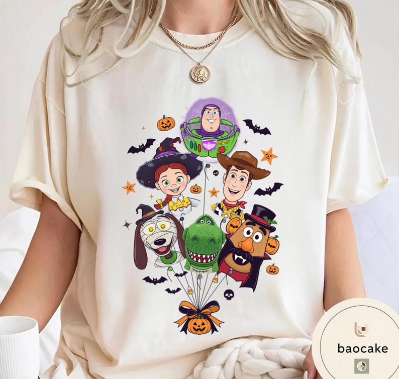 Pode incluir: Uma t-shirt de cor creme com uma impress&atilde;o gr&aacute;fica de personagens de Toy Story vestidos com fatos de Halloween, incluindo Buzz Lightyear, Woody, Jessie, Rex e o Sr. Batata, ligados por fios pretos a uma ab&oacute;bora na parte inferior.