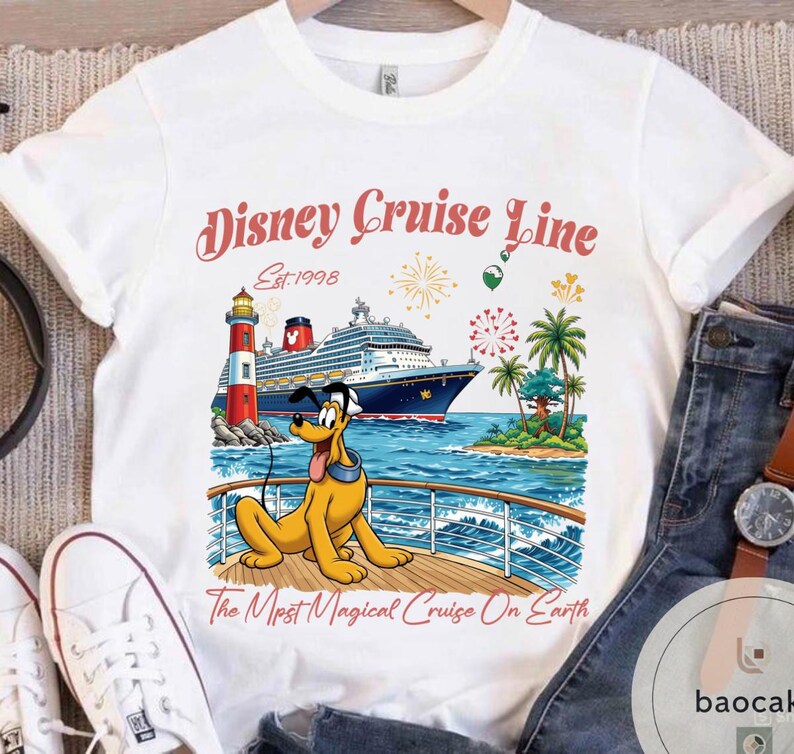 K&ouml;nnte beinhalten: Wei&szlig;es T-Shirt mit einer farbenfrohen Grafik eines Kreuzfahrtschiffs, eines Leuchtturms und Pluto. Der Text "Disney Cruise Line Est.1998" ist in einer dekorativen Schriftart dargestellt. Der Satz "The Most Magical Cruise On Earth" ist ebenfalls enthalten.