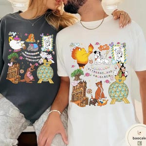 May include: Two t-shirts, one dark gray and one white, each featuring colorful cartoon character designs. The designs include various characters, flowers, and architectural elements. The white shirt has the text "Happiest Day on Earth".