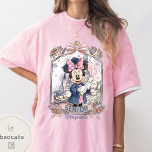 May include: Pink t-shirt featuring a Minnie Mouse graduation design. Minnie Mouse is wearing a graduation cap and gown, holding a diploma. The design includes the text "Senior Stephanie". The shirt has white sleeves.