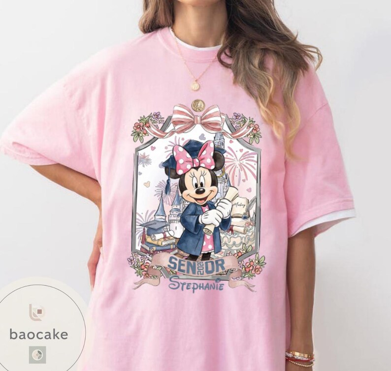May include: Pink t-shirt featuring a Minnie Mouse graduation design. Minnie Mouse is wearing a graduation cap and gown, holding a diploma. The design includes the text "Senior Stephanie". The shirt has white sleeves.