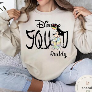 Puede incluir: Sudadera beige con la frase "Disney Soul Daddy" en negro. El dise&ntilde;o incluye un gr&aacute;fico de Mickey Mouse sosteniendo un globo arco&iacute;ris. La sudadera es de estilo casual y c&oacute;modo.