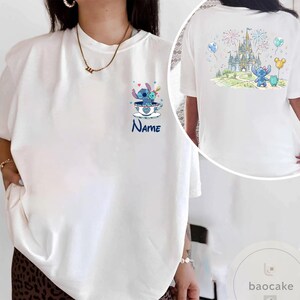 May include: White t-shirt featuring a cartoon Stitch design. The front shows Stitch in a teacup with the word "Name" below. The back displays Stitch with a castle, fireworks, and balloons. A fun, colorful design.