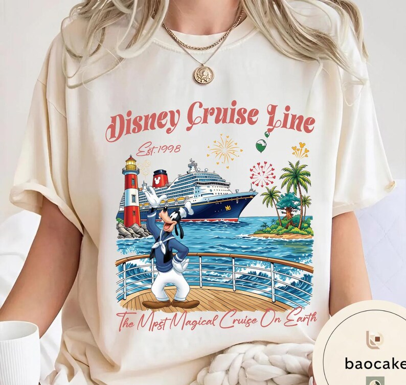 K&ouml;nnte beinhalten: Cremefarbenes T-Shirt mit einem Disney Cruise Line-Motiv. Das Design zeigt ein Schiff, Goofy, einen Leuchtturm und Palmen. Der Text lautet "Disney Cruise Line Est. 1998" und "The Most Magical Cruise On Earth."