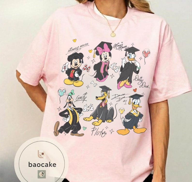May include: A light pink t-shirt featuring a graphic of Disney characters Mickey Mouse, Minnie Mouse, Donald Duck, Daisy Duck, Goofy, and Pluto in graduation attire. The shirt has the text "Mickey Mouse" and character signatures.