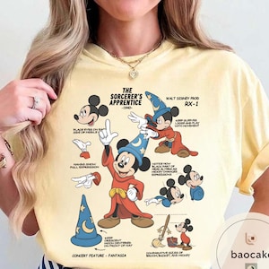 May include: A light yellow t-shirt featuring a graphic of Mickey Mouse as the Sorcerer's Apprentice from Fantasia. The design includes illustrations and text detailing the character's features and the film's production. The text reads "The Sorcerer's Apprentice - 1940".