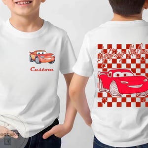 May include: White t-shirt featuring a cartoon image of a red race car with the text "Custom" on the front. The back of the shirt has a red and white checkered pattern with the words "Lightning McQueen" and a red race car.