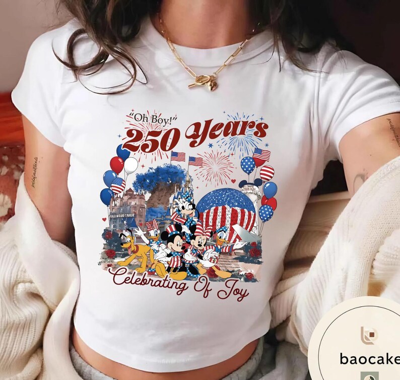 Puede incluir: Camiseta blanca con un gr&aacute;fico colorido que celebra 250 a&ntilde;os. El dise&ntilde;o incluye a Mickey Mouse, Minnie Mouse, Donald Duck y otros personajes de Disney, junto con fuegos artificiales, globos y banderas americanas. El texto incluye "Oh Boy!" y "Celebrating of Joy."