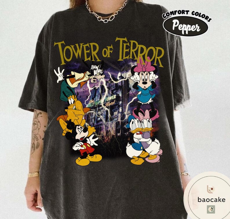 May include: Dark gray t-shirt featuring the text "TOWER OF TERROR" in yellow, with cartoon characters. The shirt has a distressed look and a "Comfort Colors Pepper" logo.