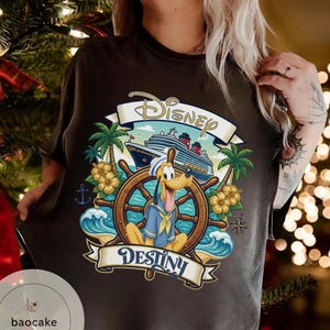 May include: Dark brown t-shirt featuring a colorful Disney design. The graphic includes Pluto at a ship's wheel, a cruise ship, palm trees, and the words "Disney" and "Destiny" in a banner.