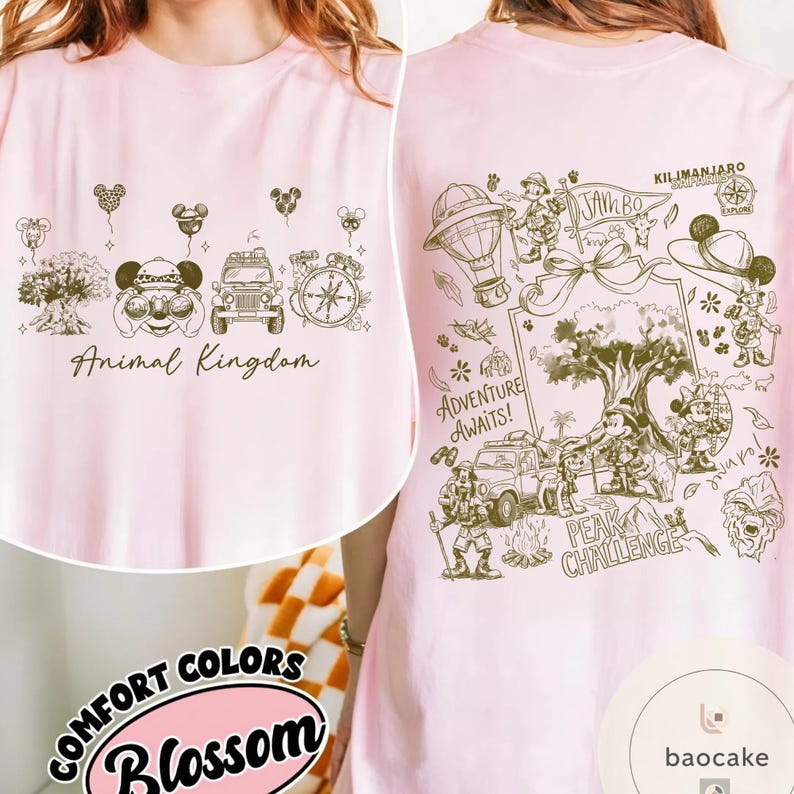 May include: A light pink t-shirt with a front graphic of Animal Kingdom icons and text. The back features a detailed illustration with the text "Adventure Awaits!" and "Peak Challenge". The shirt is labeled "Comfort Colors Blossom".