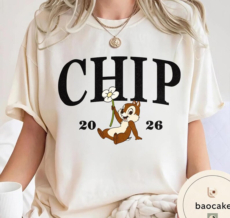 May include: Cream-colored t-shirt featuring the word "CHIP" in large black letters above a cartoon chipmunk holding a flower. The numbers "20" and "26" flank the chipmunk. The shirt has short sleeves.
