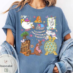 May include: A blue t-shirt featuring various cartoon characters and icons. The shirt includes images of a teapot, dogs, cats, a kangaroo, and a building. The text "Happiest Mom on Earth" is also present.