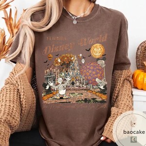 Op de afbeelding: Bruin T-shirt met een Halloween-thema Disney World-afbeelding. Het ontwerp bevat een mummie, pompoenen, een kasteel en de tekst "Florida Disney World" en "The Most Spooked Place On Earth."
