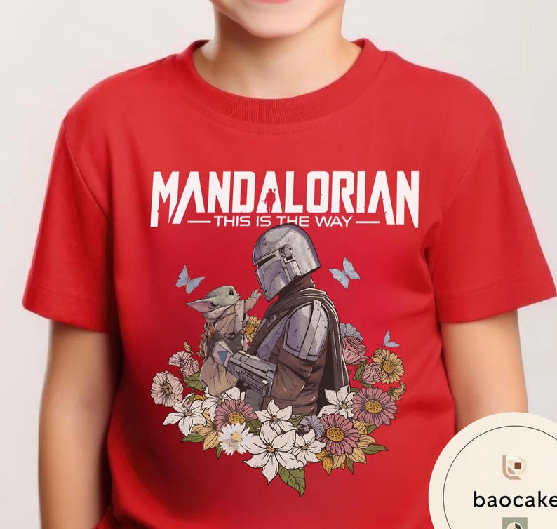 Puede incluir: Camiseta roja con un dise&ntilde;o de The Mandalorian y Grogu rodeados de flores y mariposas. El texto "MANDALORIAN - THIS IS THE WAY" est&aacute; impreso en blanco en la parte superior.