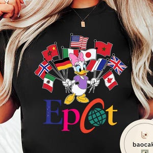 May include: Black t-shirt with a cartoon of Daisy Duck holding flags from different nations. The word "Epcot" is printed in colourful letters below the character, with a globe graphic. A fun and colourful design.