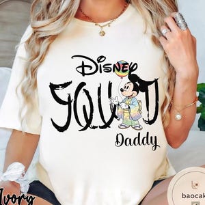 Puede incluir: Camiseta de color marfil con el texto "Disney YOU Daddy" en escritura negra. El dise&ntilde;o incluye un personaje de dibujos animados de Mickey Mouse sosteniendo un globo arco&iacute;ris. La camiseta es una prenda informal.