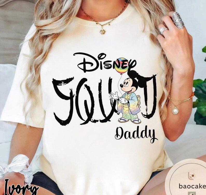 Puede incluir: Camiseta de color marfil con el texto "Disney YOU Daddy" en escritura negra. El dise&ntilde;o incluye un personaje de dibujos animados de Mickey Mouse sosteniendo un globo arco&iacute;ris. La camiseta es una prenda informal.