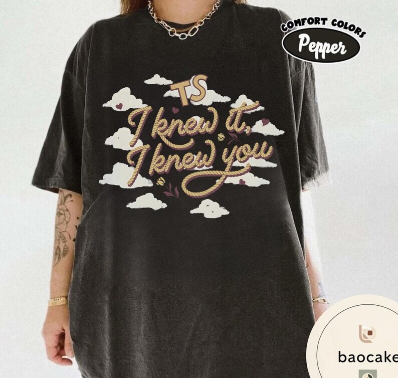 K&ouml;nnte beinhalten: Ein anthrazitfarbenes Kurzarm-T-Shirt mit einem Grafikdruck aus wei&szlig;en Wolken, kleinen Herzen und dem Text TS I knew it, I knew you in einer seilartigen Schriftart. Das T-Shirt hat ein Comfort Colors Pepper-Etikett in der oberen rechten Ecke.