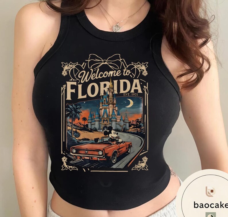 May include: Black tank top with a graphic featuring a vintage Florida travel design. The design includes a castle, Mickey Mouse in a red convertible, and the text "Welcome to Florida, Est. 1971."