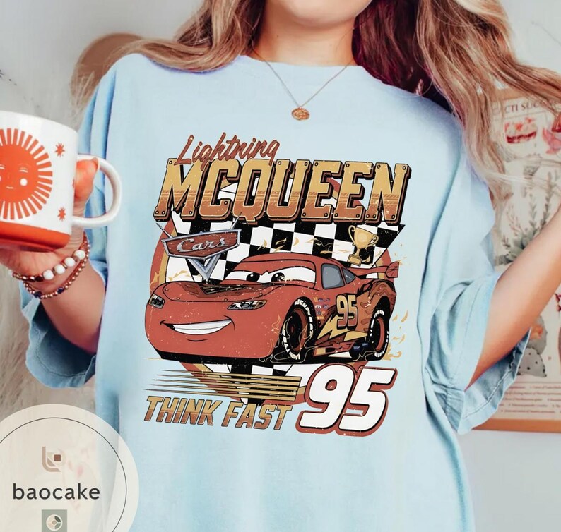 Puede incluir: Camiseta azul claro con un dise&ntilde;o de Rayo McQueen de la pel&iacute;cula Cars. El dise&ntilde;o incluye el texto "Lightning McQueen", "Cars", "Think Fast" y el n&uacute;mero "95". La camiseta tiene un aspecto vintage y desgastado.