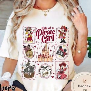 May include: Ivory-colored t-shirt featuring a "Life of a Pirate Girl" design. The design includes cartoon pirate characters, a treasure chest, a ship, a castle, and other pirate-themed elements. The text "Life of a Pirate Girl" is in a decorative font.