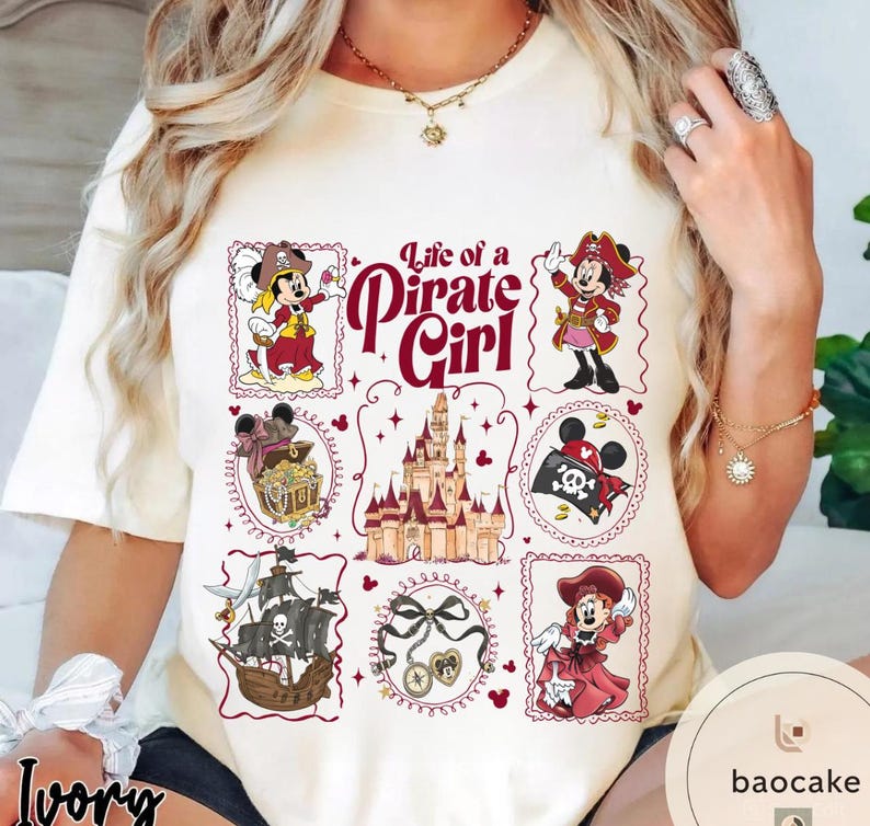 May include: Ivory-colored t-shirt featuring a "Life of a Pirate Girl" design. The design includes cartoon pirate characters, a treasure chest, a ship, a castle, and other pirate-themed elements. The text "Life of a Pirate Girl" is in a decorative font.