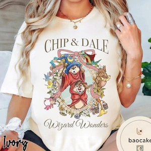 May include: Ivory-colored t-shirt featuring Chip and Dale characters in a floral wreath with the text "Chip & Dale Wizard Wonders." The design includes Chip and Dale in wizard attire, surrounded by colorful flowers and a pink bow.