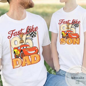 May include: White t-shirts with a cartoon car graphic. The shirts have the text "Fast Like Dad" and "Fast Like Son" in a vintage style. The car is red with yellow accents, a trophy, and a checkered flag.
