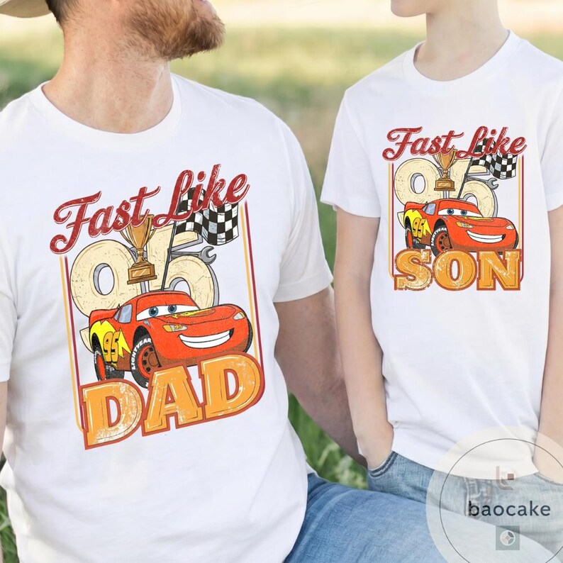 May include: White t-shirts with a cartoon car graphic. The shirts have the text "Fast Like Dad" and "Fast Like Son" in a vintage style. The car is red with yellow accents, a trophy, and a checkered flag.