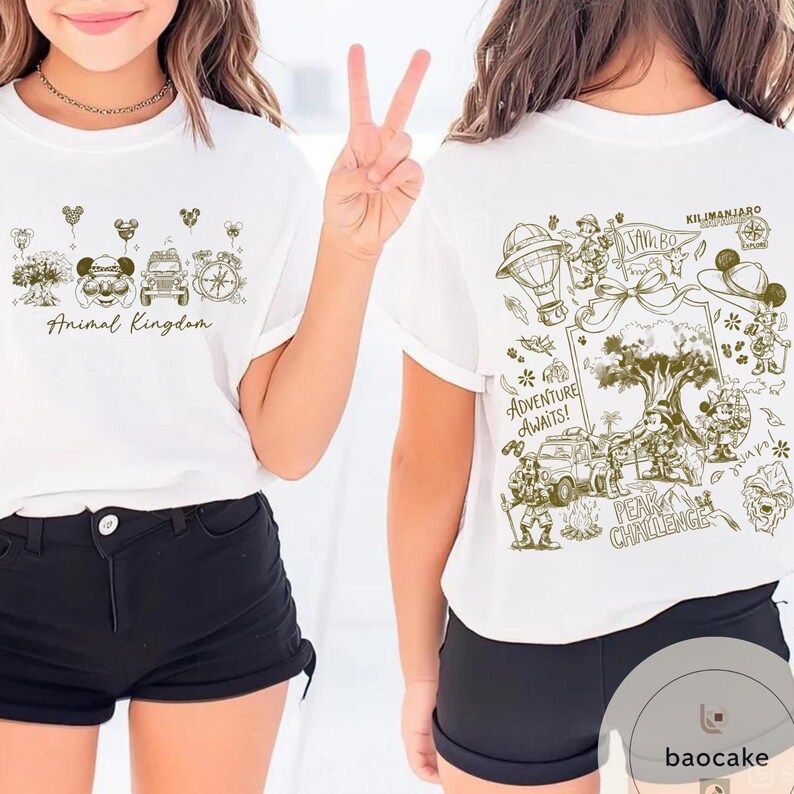May include: White t-shirts with green and brown illustrations. One shirt features "Animal Kingdom" text and cartoon images. The other shirt has "Kilimanjaro" text and a detailed adventure scene with a hot air balloon and characters.